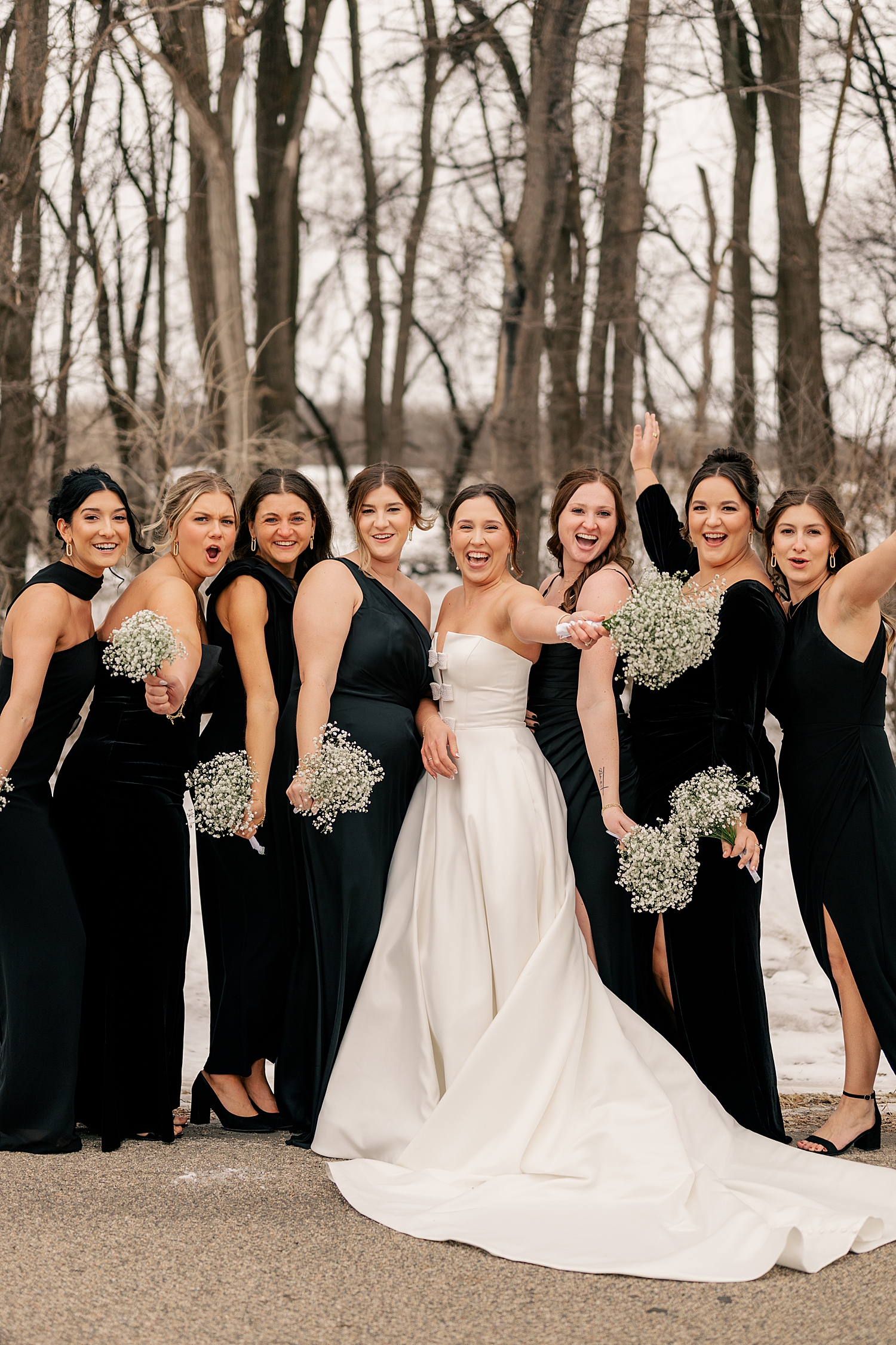 bridesmaids in black dresses surround bride outside for Wintry Minnesota Wedding