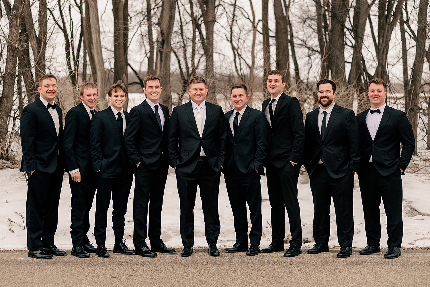 groomsmen in suits stand outside in the snow for Wintry Minnesota Wedding