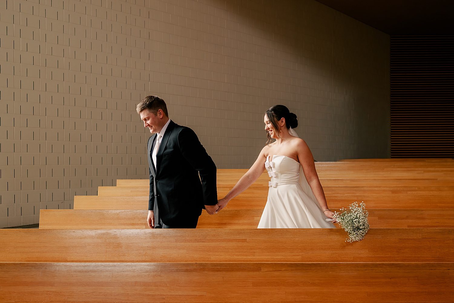 husband and wife walk hand in hand down a pew in church by Rule Creative Co