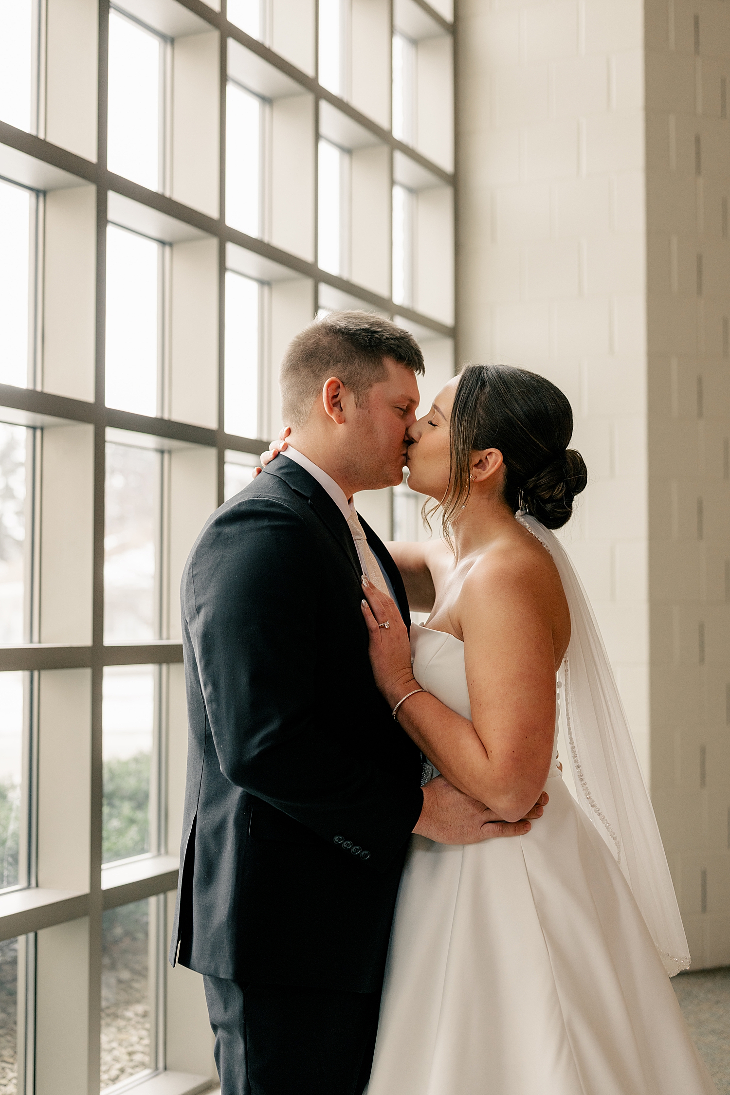 couple share a kiss next to oversized church windows by MN elopement photographer