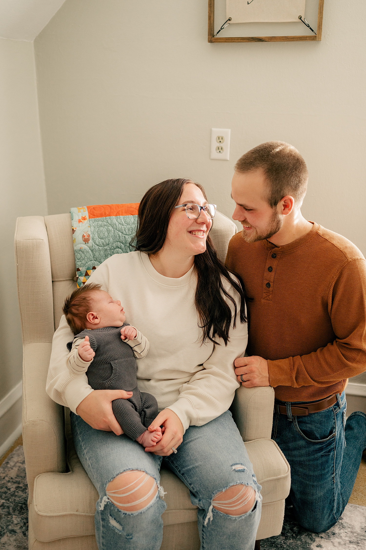 mother in denim and white sits in rocker looking at her husband by Rule Creative Co