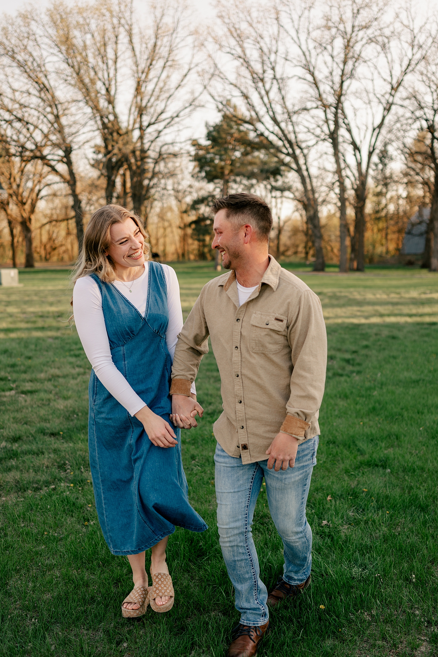 couple runs hand in hand through field for summer engagement photos