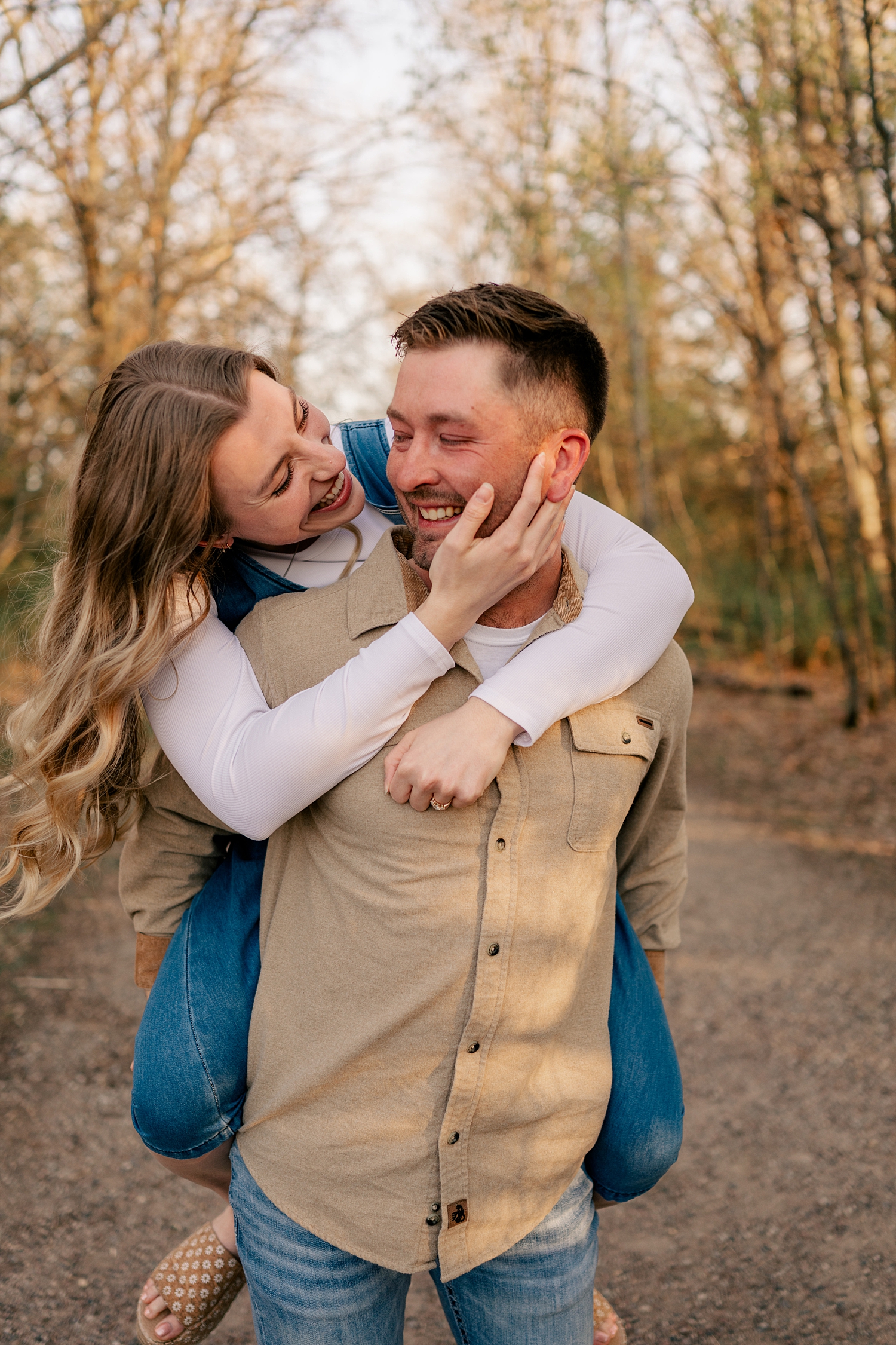 woman hops on her fiancé's back as they laugh under the trees by Rule Creative Co