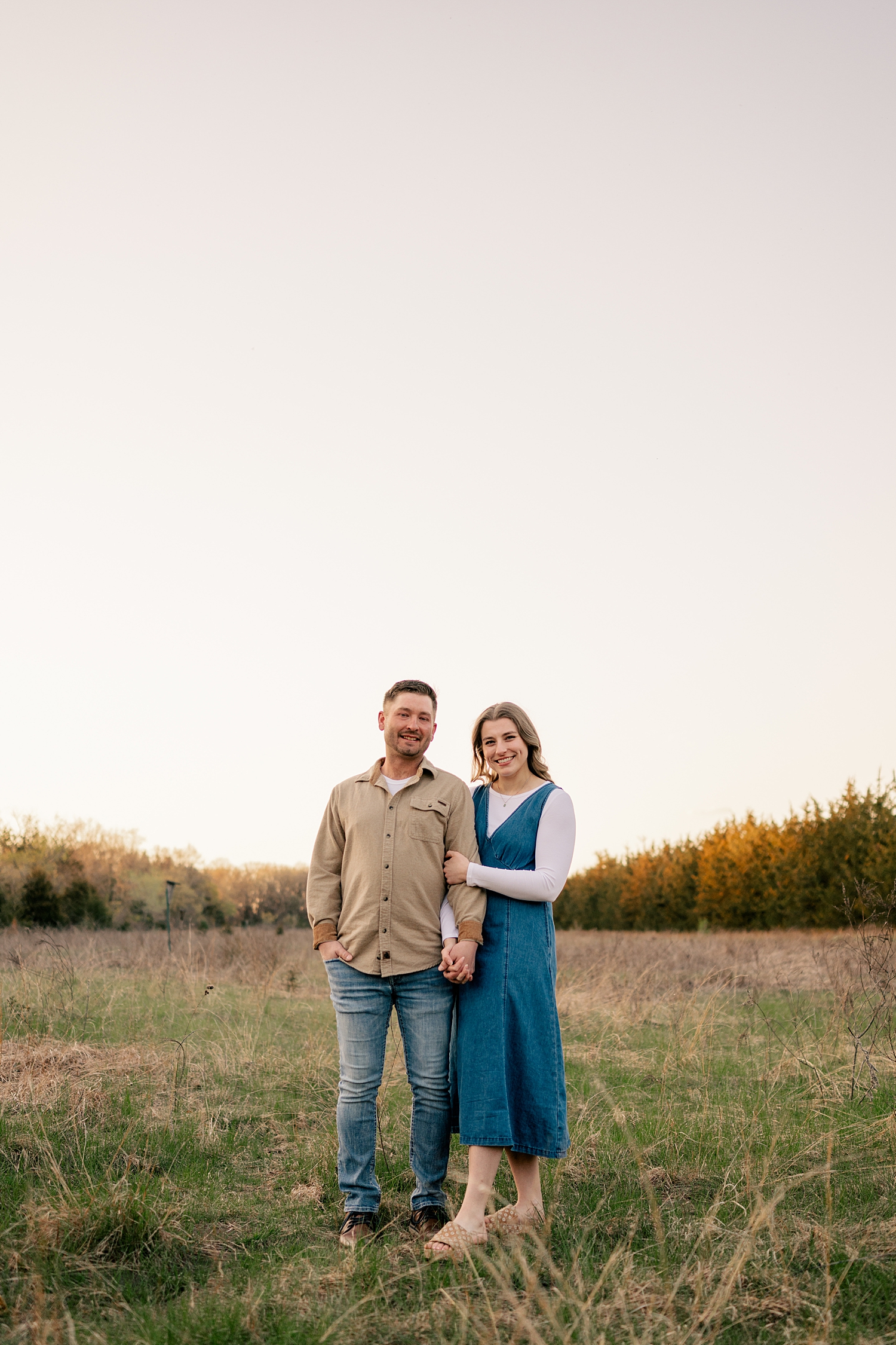 couple snuggle in field during golden hour for summer engagement photos