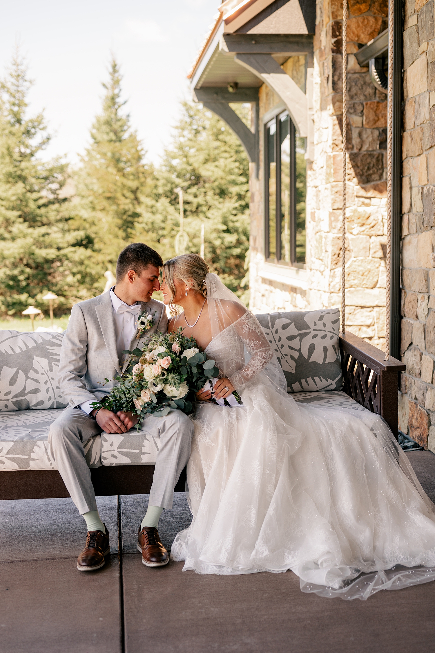 husband and wife sit on porch bench on their big day by Minnesota wedding photographer