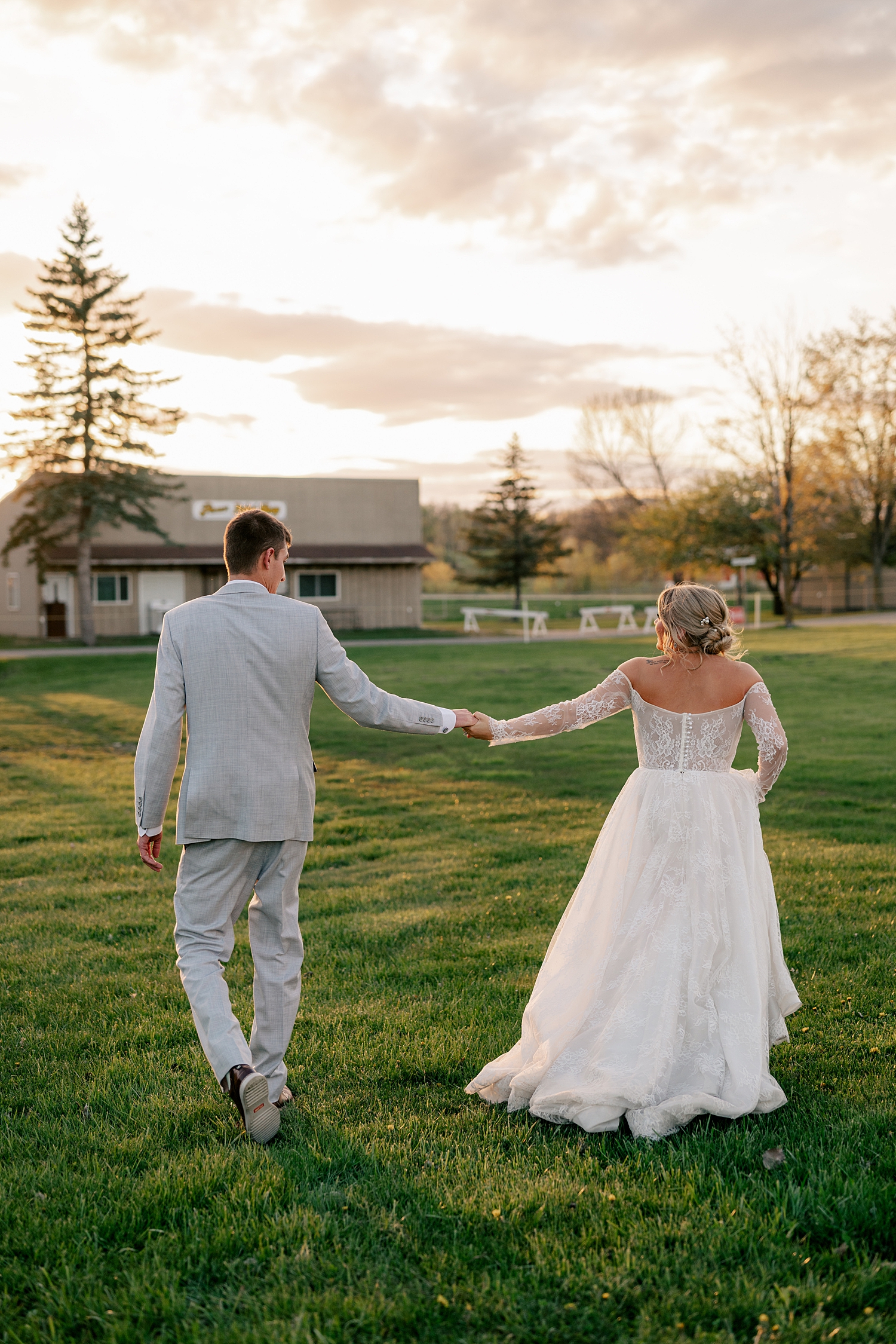 man and woman walk hand in hand through field at golden hour by Rule Creative Co 