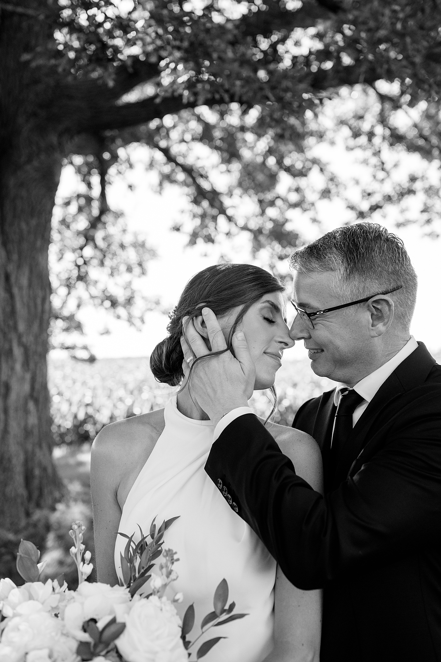 newlyweds lead in for a kiss under big tree by MN wedding photographer