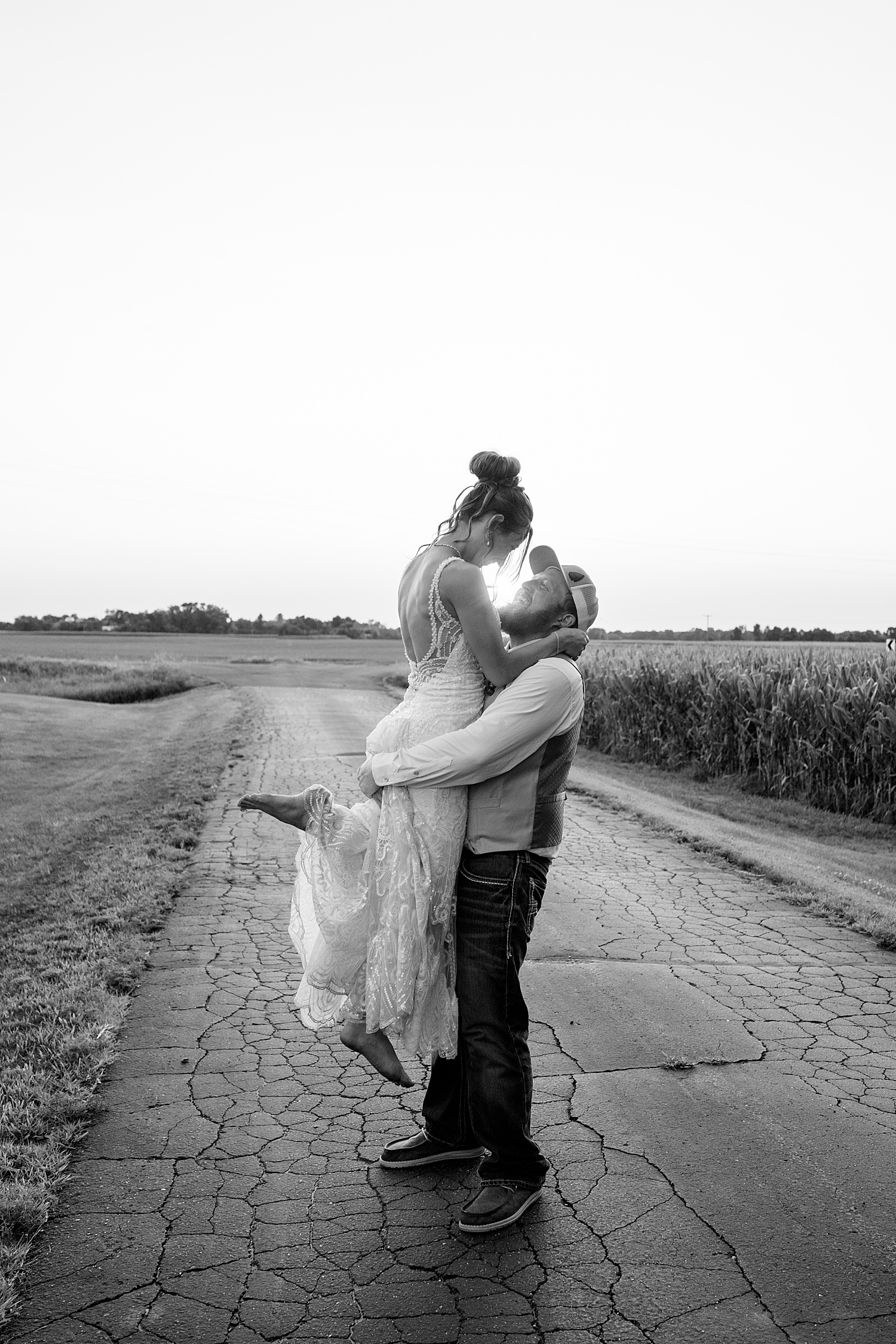 man lifts up his new bride on street for red barn wedding