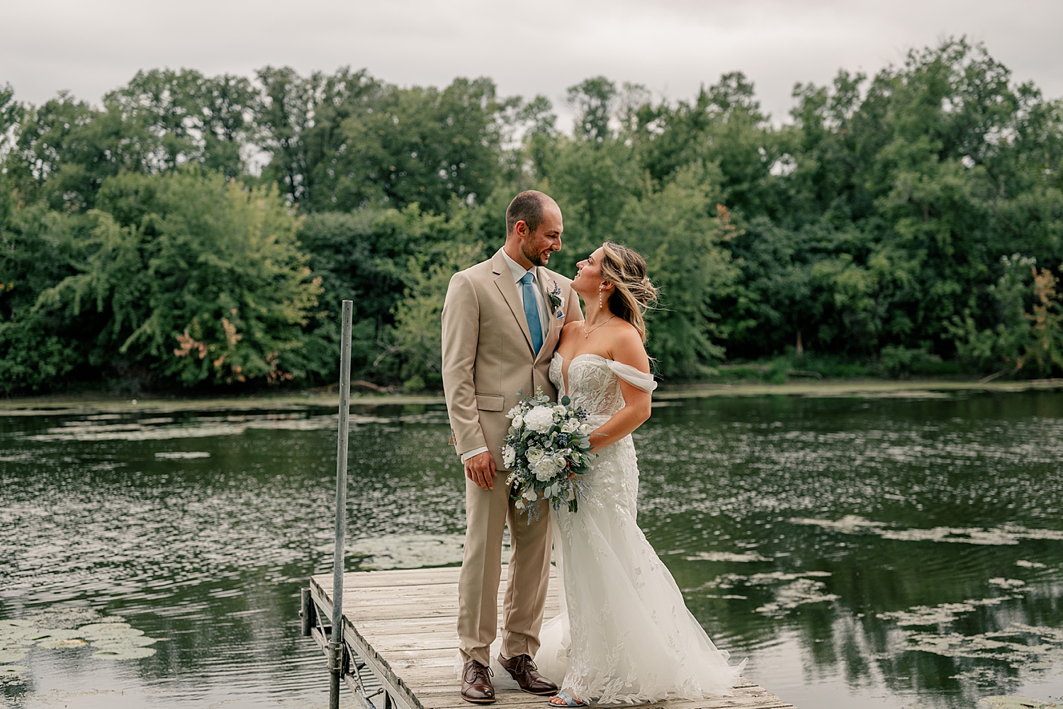 newlyweds stand on dock over water by Minnesota photographer