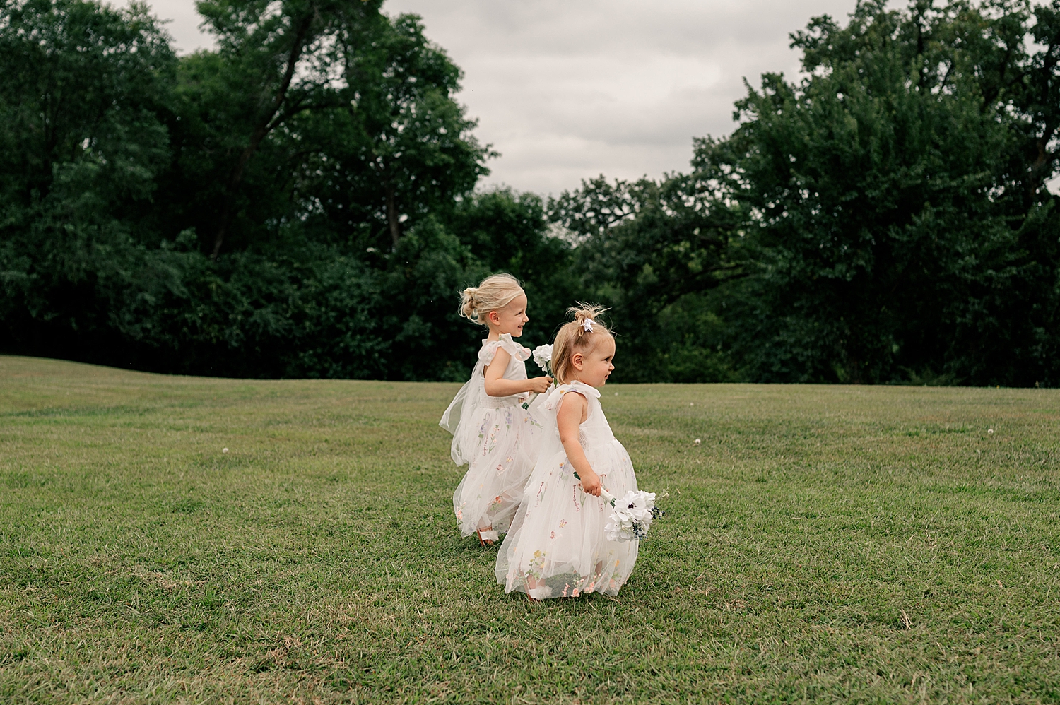 small toddler flower girls walk across a field for a family-friendly wedding